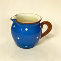 Blue ceramic pitcher with white polka dots and brown handle on a beige background
