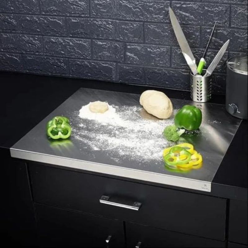 Stainless steel kitchen countertop with vegetables and a flour container against a dark tiled wall.